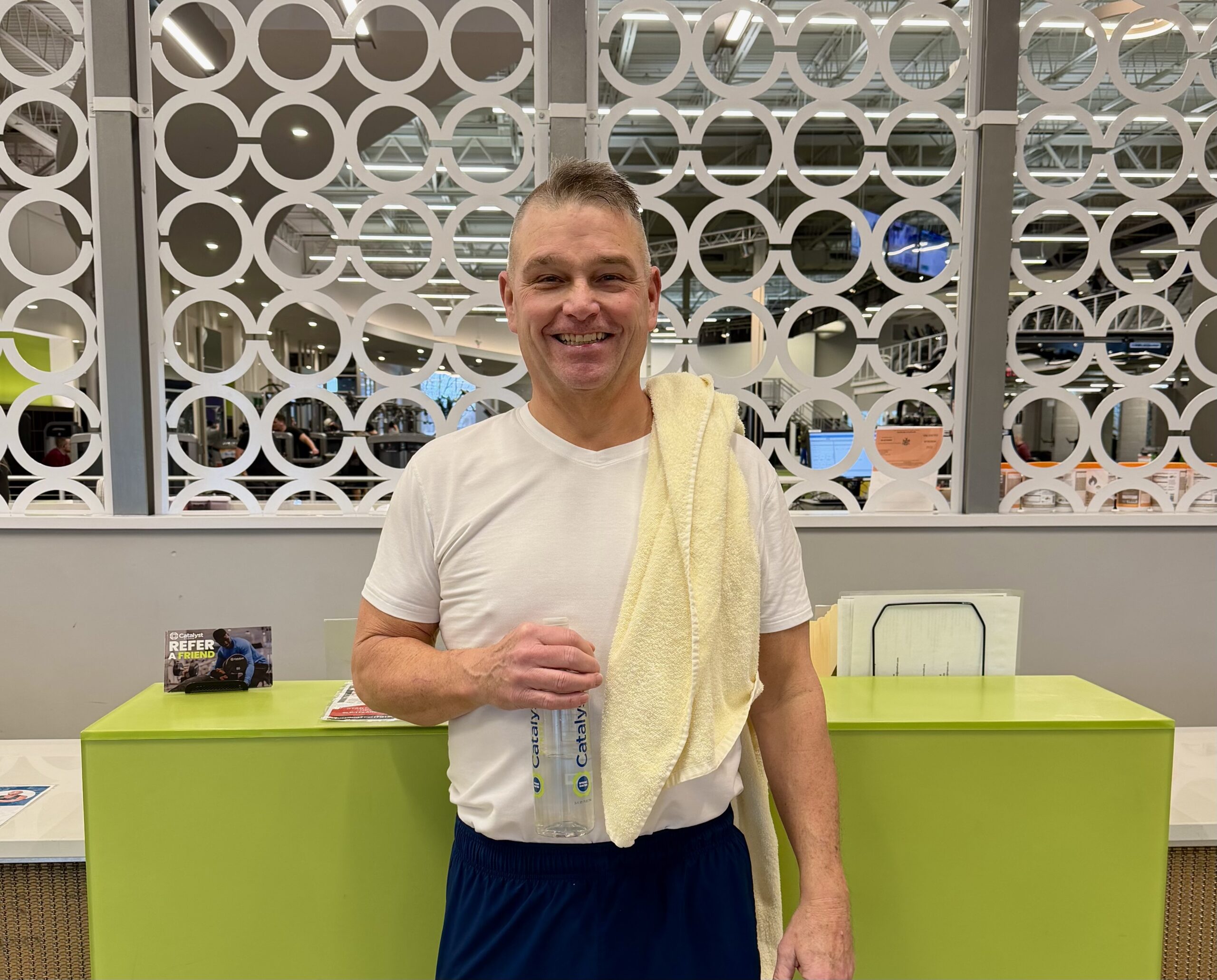 Man smiling and holding a Catalyst Water with a towel on his shoulder.
